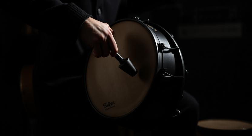 Person learning how to play the bodhrán in a dark folk setting